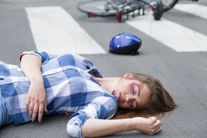 Young woman lying hurt on the road with her bike and helmet at the background